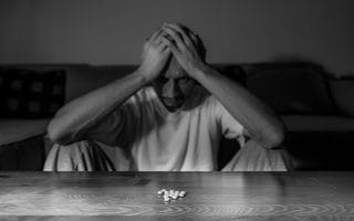 An Addict Sitting on the Floor Facing Pills on a Wooden Table